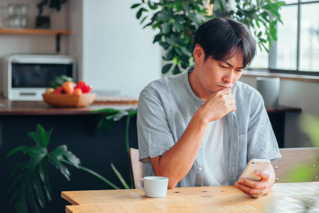 スマートフォンを見て悩んでいる男性