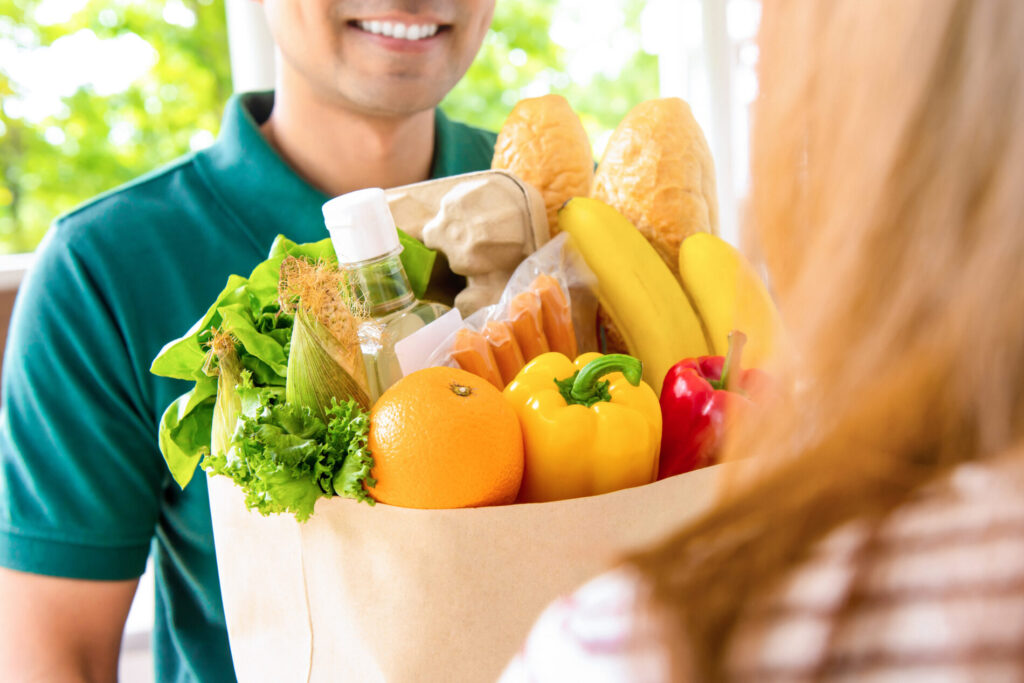 紙袋に入った食材を笑顔で手渡す男性