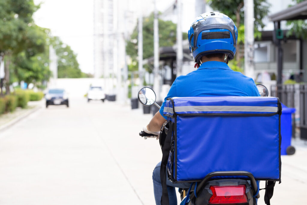 青い配達バックをバイクに載せ走行している男性