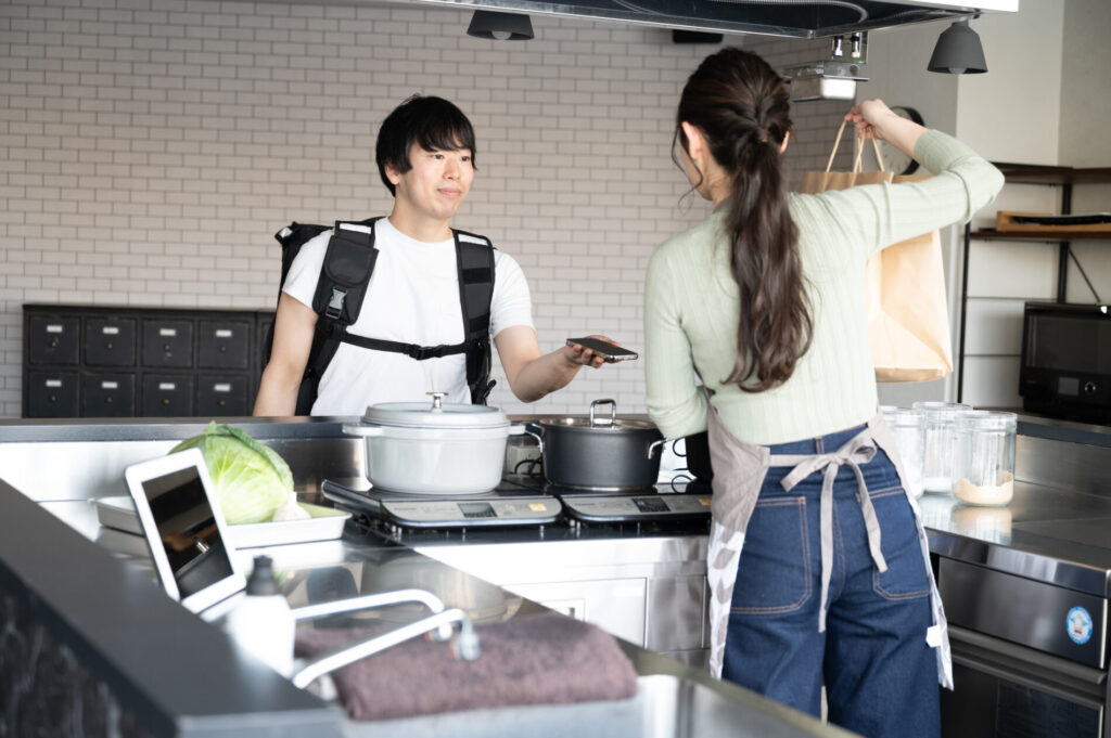 飲食店スタッフにスマホを見せている配達員男性